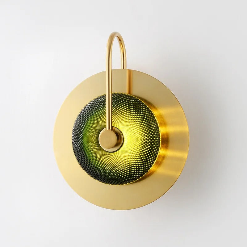 Brass wall sconce with a green textured glass disc on a curved arm