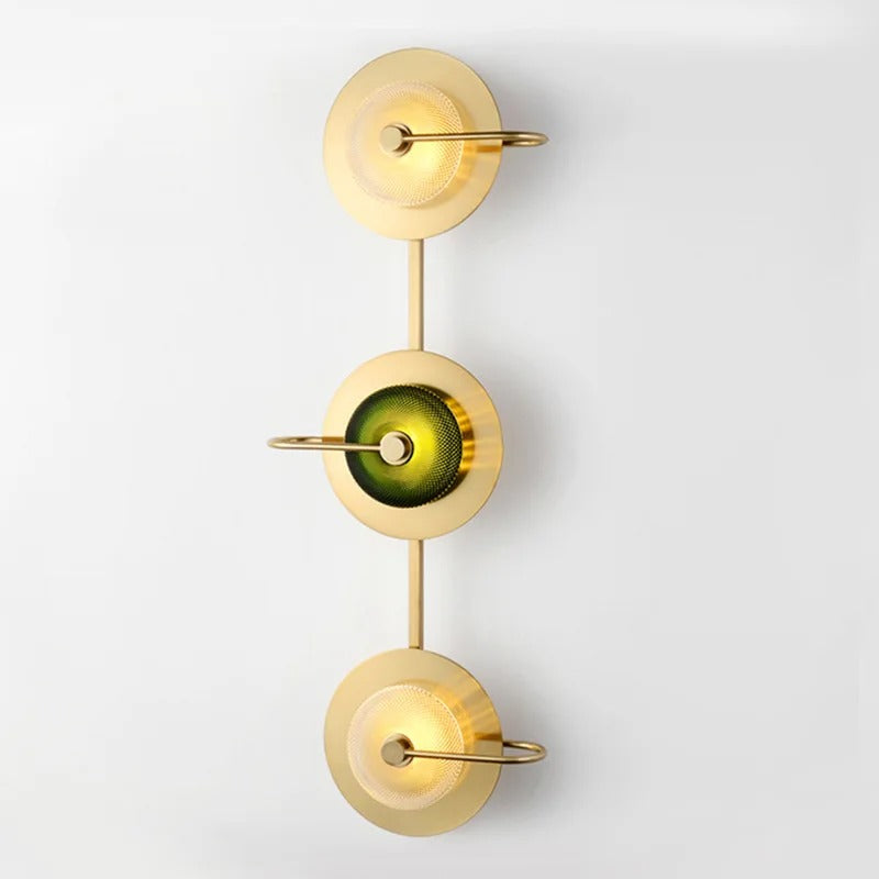 Three light brass sconce with green glass discs running down a white wall
