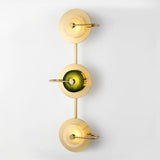 Three light brass sconce with green glass discs running down a white wall