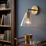 Cone shade sconce lit warm beside a bookcase and a brass bar cart