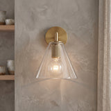 Bronze wall sconce with a clear glass cone shade on a plaster wall
