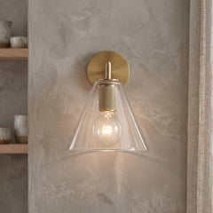 Bronze wall sconce with a clear glass cone shade on a plaster wall