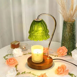 Green glass candle warmer lamp on a white table surrounded by pale roses