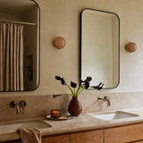 Pair of caramel glass wall sconces flanking mirrors above a stone vanity