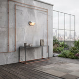 Bronze bulkhead lamp mounted on a pale render wall beside a rooftop terrace