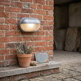 Silver bulkhead lamp on a red brick wall above a terracotta pot and step