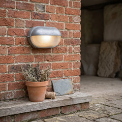 Silver bulkhead lamp on a red brick wall above a terracotta pot and step