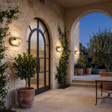 Bulkhead lamps flanking an arched black door on a stone garden terrace