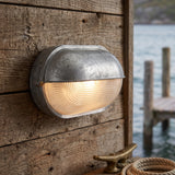 Galvanised oval bulkhead lamp with ribbed lens on weathered timber cladding