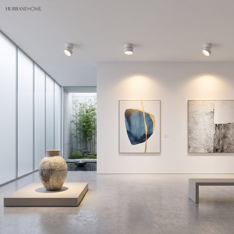 White ceiling spot lights angled at framed artwork in a bright gallery room