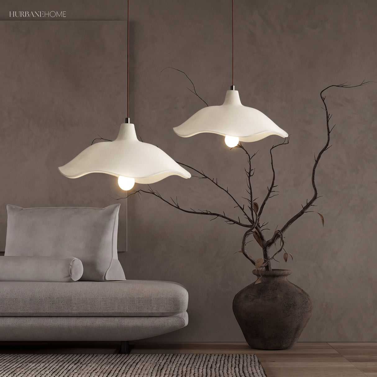 Two cement flower pendant lights above a grey sofa with bare branches