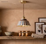 Striped ceramic pendant lit above a shelf of pots and candles