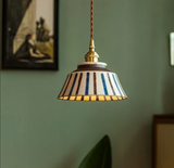 Striped ceramic pendant lit warm against a green painted wall