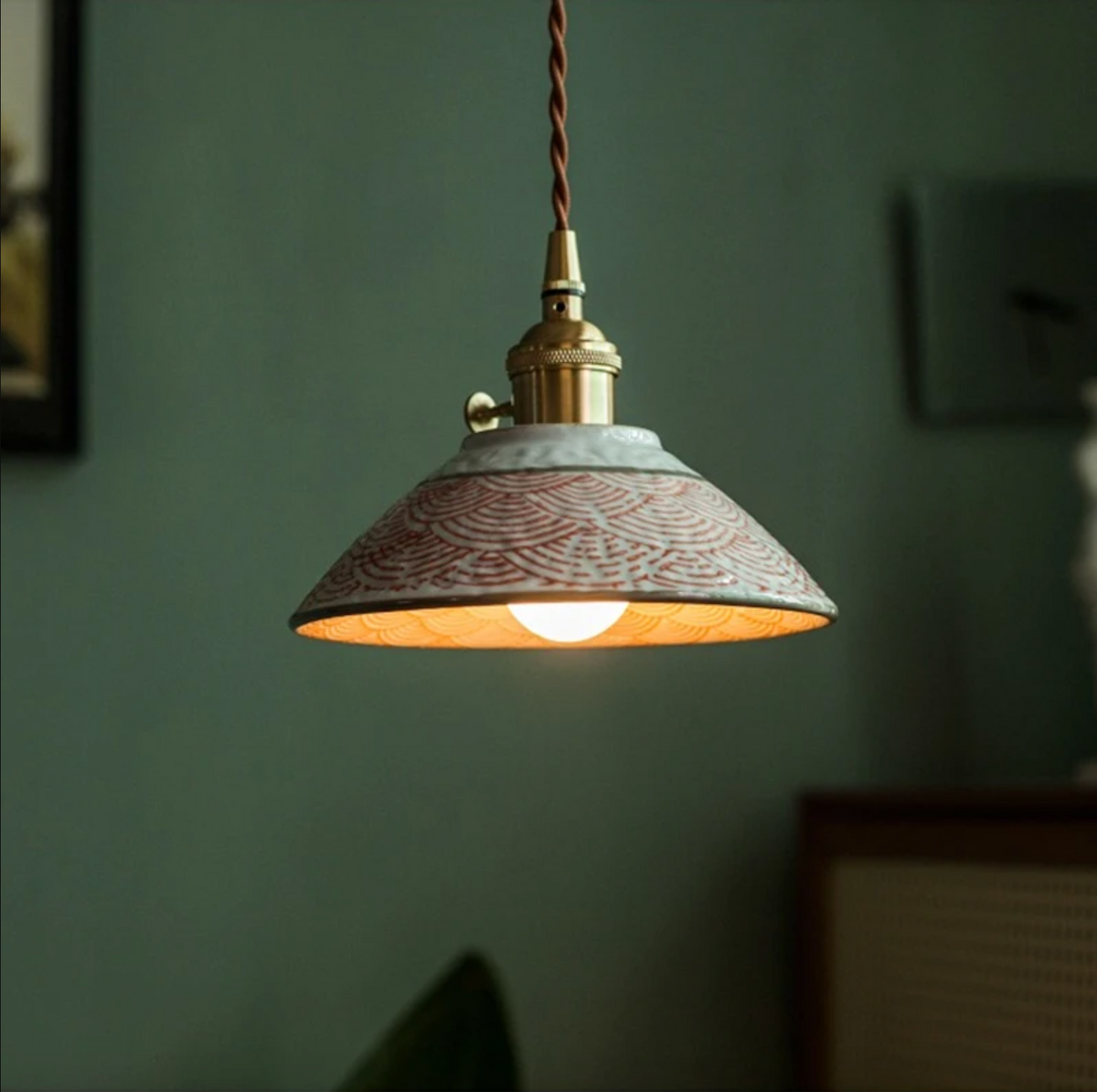 Textured ceramic pendant glowing warm on a green wall