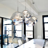 Chrome molten pendants above a bright kitchen bar with tall windows behind