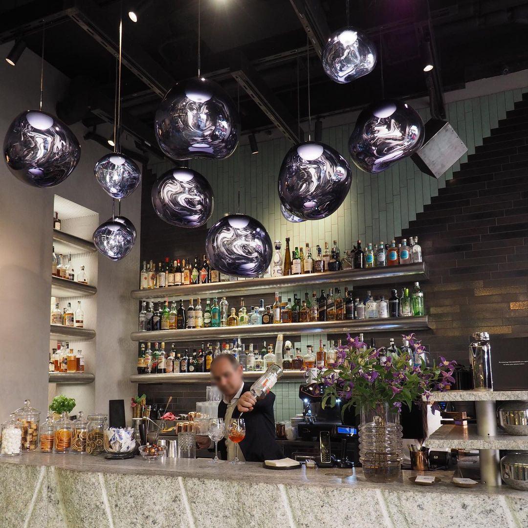 Row of chrome molten pendants above a cocktail bar with a bartender pouring