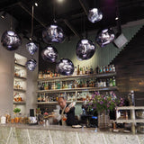 Row of chrome molten pendants above a cocktail bar with a bartender pouring