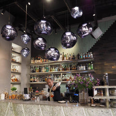 Row of chrome molten pendants above a cocktail bar with a bartender pouring