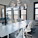 Line of chrome molten pendants above a long white office meeting table
