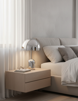 Chrome dome lamp lit on a bedside cabinet next to a made white bed