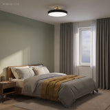 Black circular ceiling light above a bed in a green toned bedroom