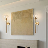 Clear glass globe wall sconce on a brass stem front view