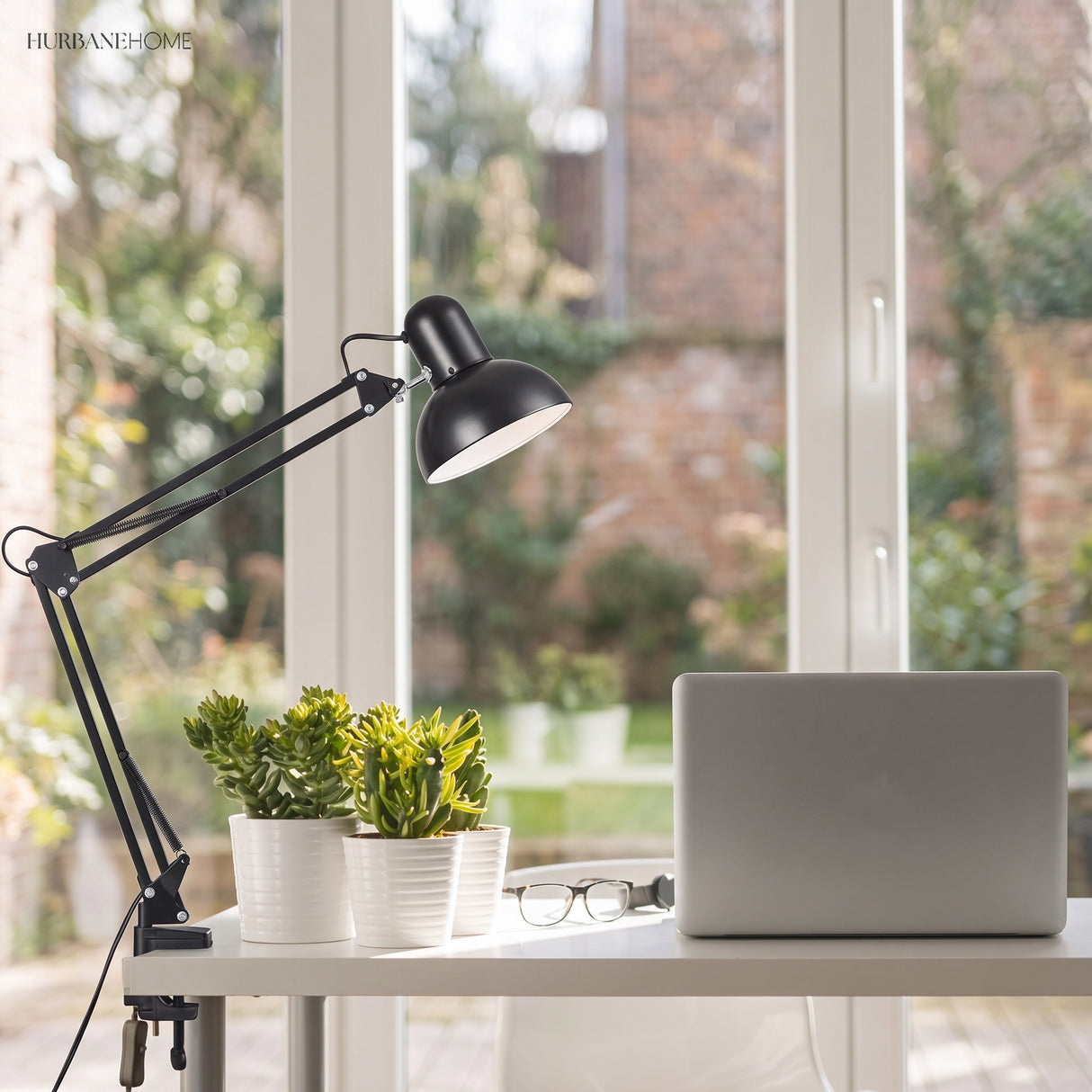 Black clip-on swing arm lamp on a white desk beside a laptop and plants