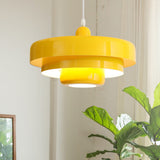 Yellow tiered pendant light hanging by a bright window next to a leafy plant