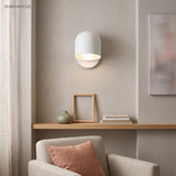 White macaron wall sconce lit above a shelf in a living room