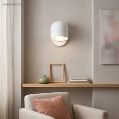 White macaron wall sconce lit above a shelf in a living room