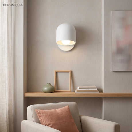 White macaron wall sconce lit above a shelf in a living room