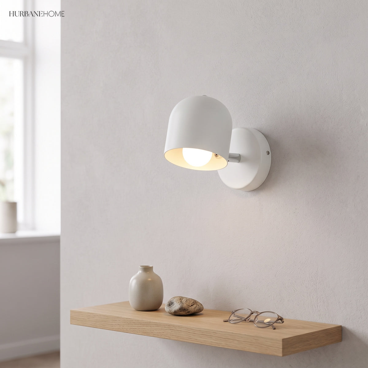 White macaron sconce lit on a plain wall above an oak shelf