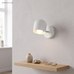 White macaron sconce lit on a plain wall above an oak shelf