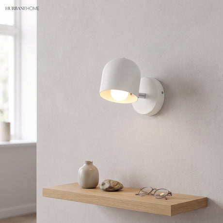 White macaron sconce lit on a plain wall above an oak shelf