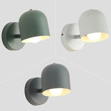 White macaron sconce lit above a bedside cabinet and alarm clock