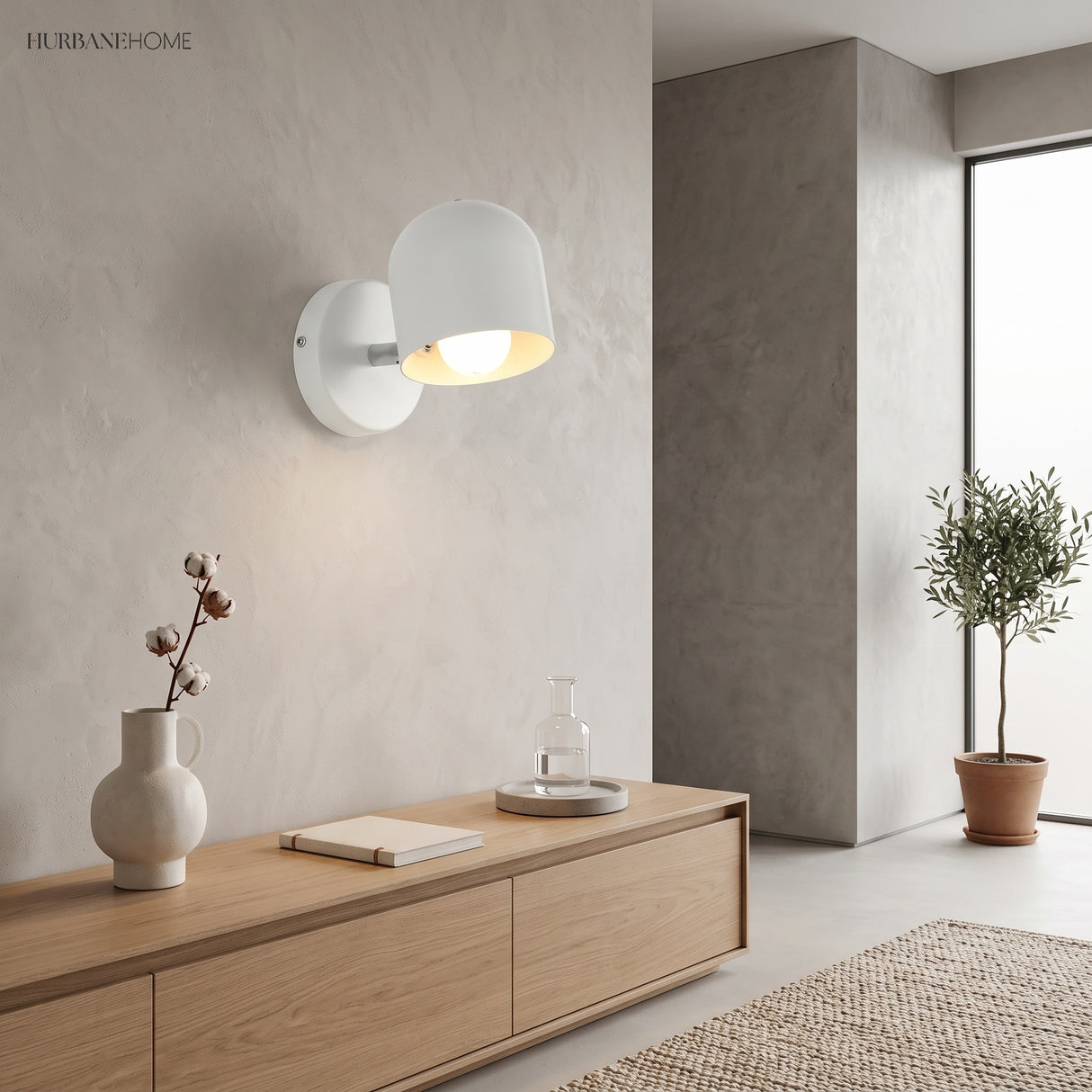 White dome sconce lit above a sideboard beside a potted olive tree