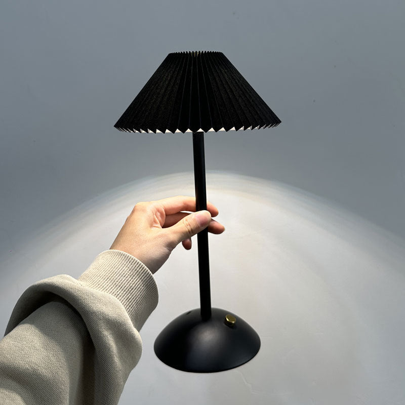 Hand holding the slim black cordless table lamp by its stem