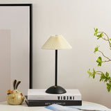 Black base table lamp with cream pleated shade beside books