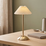 Gold pleated table lamp lit on a wood side table at dusk