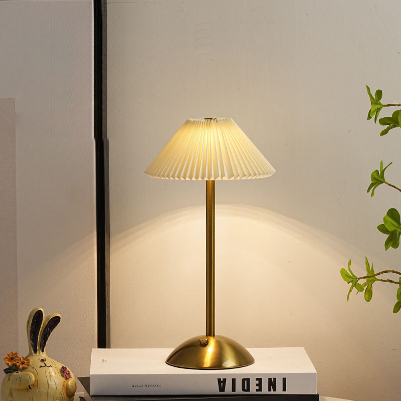 Gold pleated table lamp with cream conic shade on a white studio background