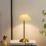 Gold pleated table lamp with cream conic shade on a white studio background