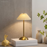 Lit gold cordless table lamp on white books beside a vase and greenery
