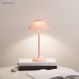 Pink pleated table lamp glowing warm with a control button on its domed base