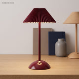 Red pleated table lamp on a wood desk with a base control knob