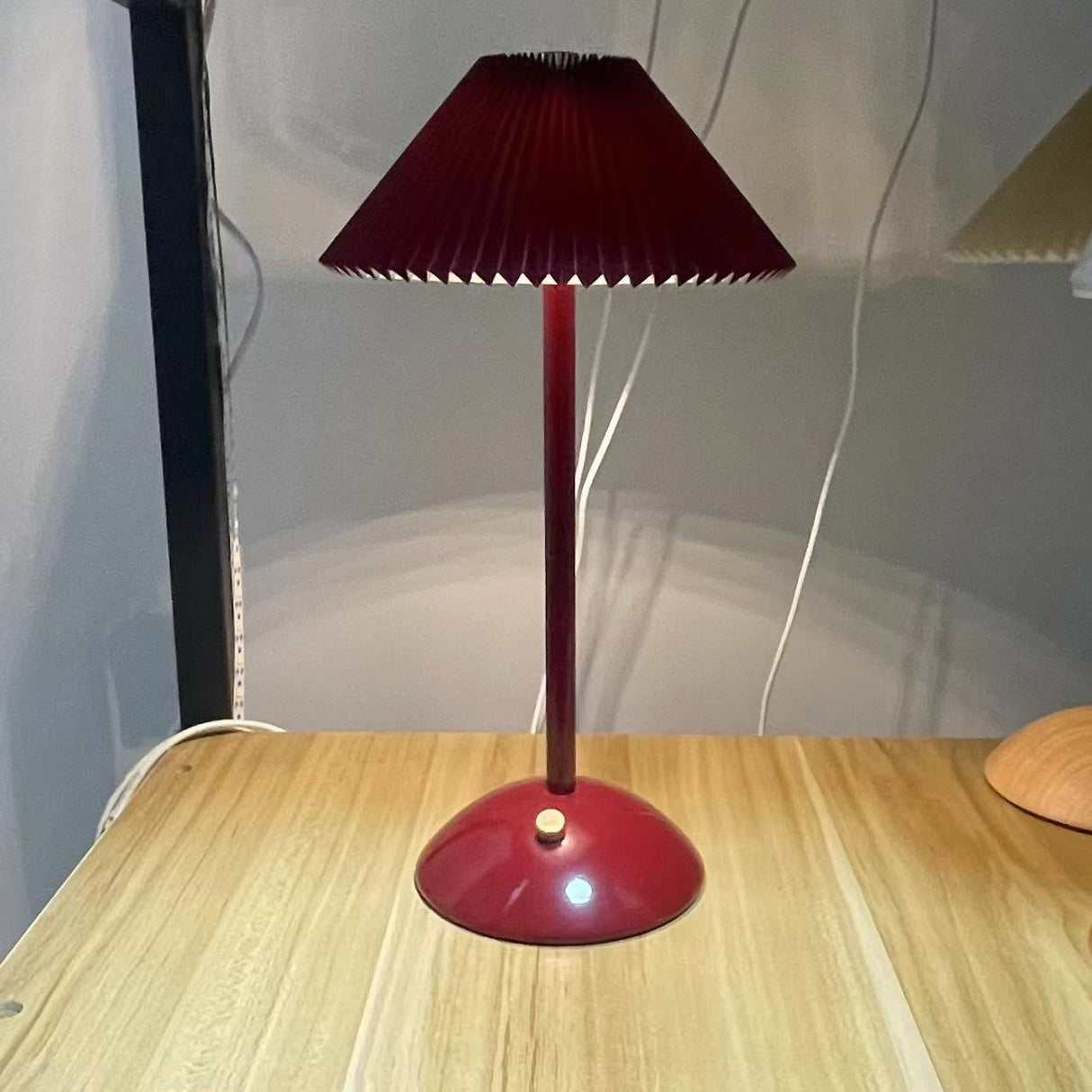Deep red table lamp on a wood table with a base mounted button