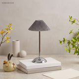 Chrome base lamp with grey conic pleated shade on stacked books