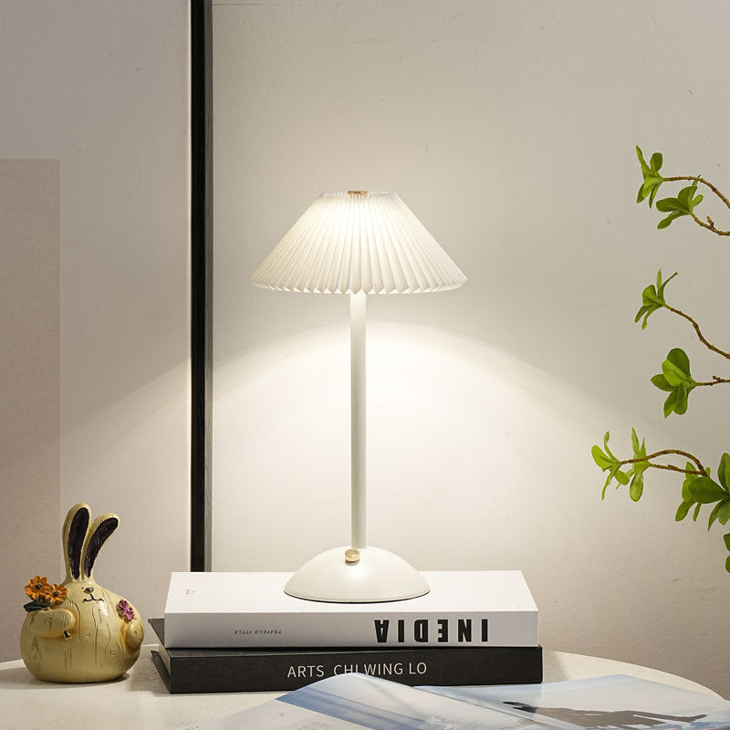 White table lamp lit on a stack of books at a cosy bedside