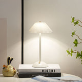 White table lamp lit on a stack of books at a cosy bedside