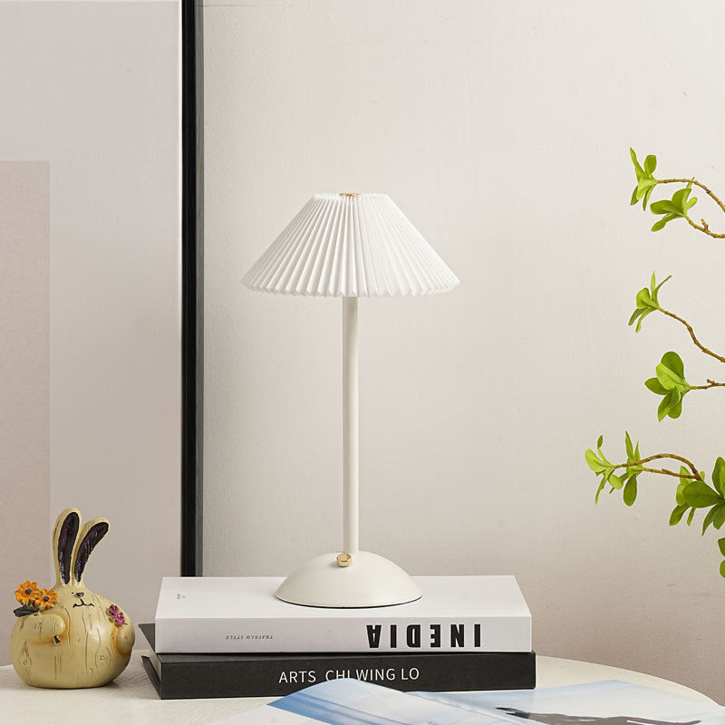 All white table lamp with pleated shade styled on a bright shelf