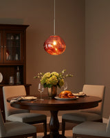 Copper pendant lit above a round dining table beside a dark glazed cabinet